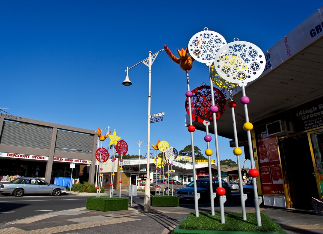 Large colourful Christmas sculptures (baubles, stars and birds) stand tall over the pavement in Noble Park's main street.