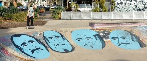 Photo of a persona skating in Prahran. A large mural of blue men is painted on the skate ramp.