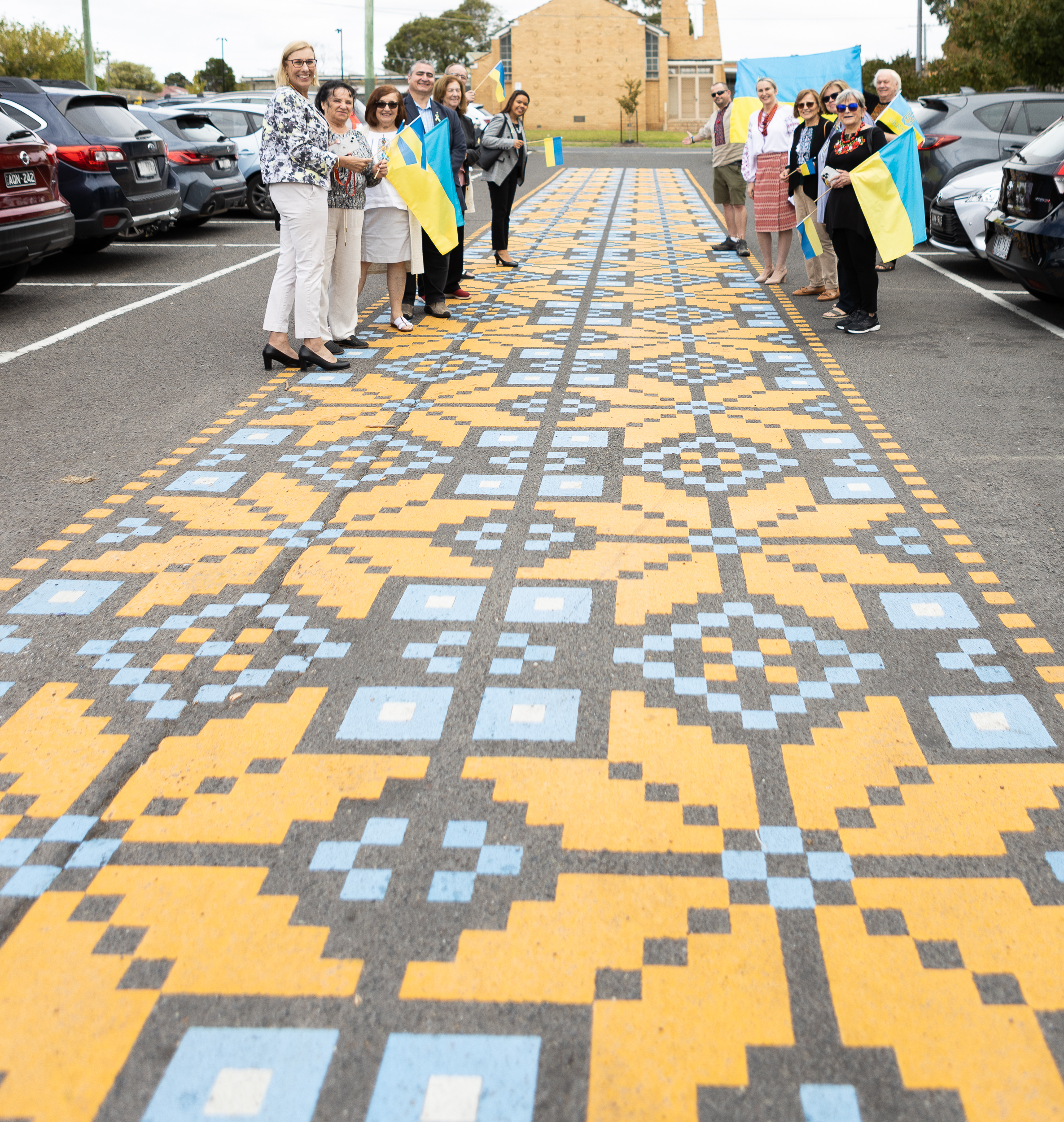 People standing next to Ukrainian mural painted on the road