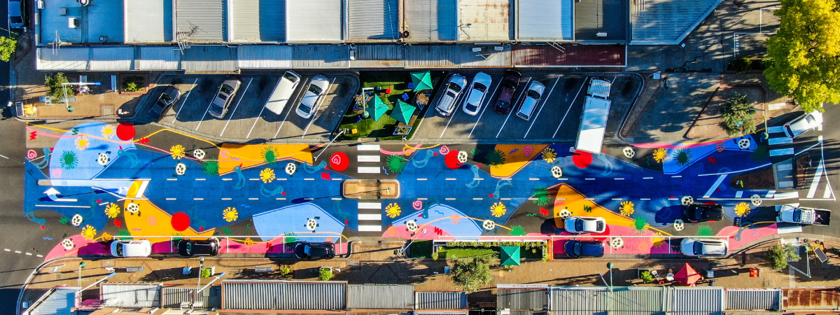 Aerial photograph of a shopping strip where the road has been painted with colourful murals